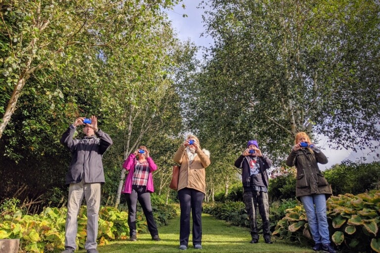 Open Aye. a group of people standing in front of the camera taking photographs in a forest.