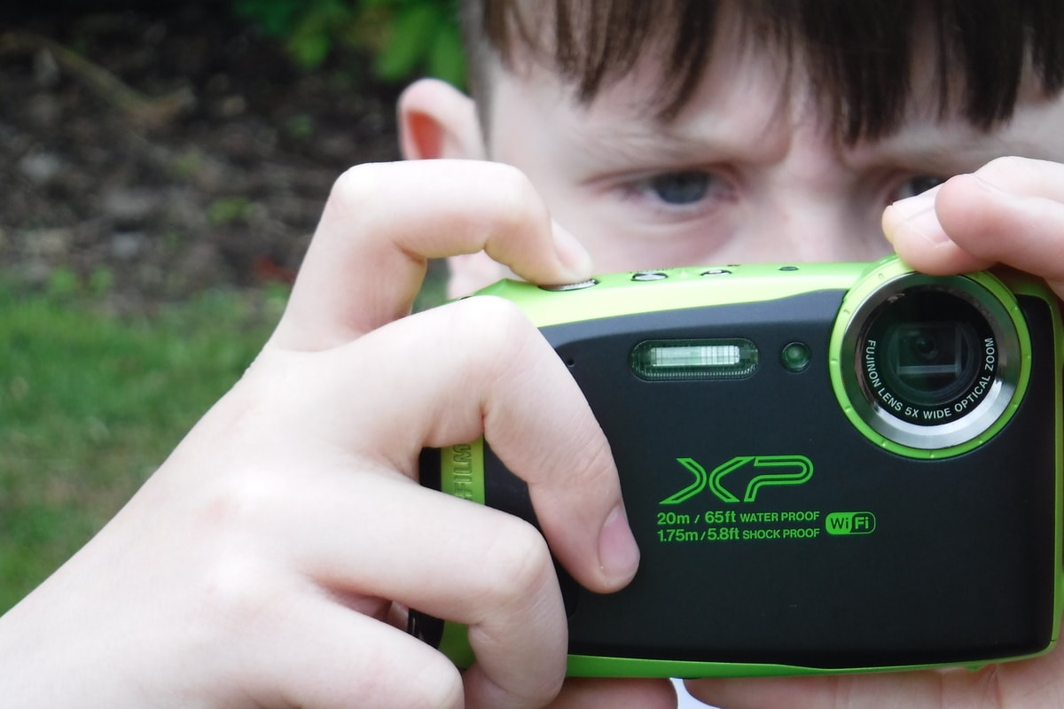 Open Aye. Photo of a boy taking a photo with a green digital camera in a natural setting.